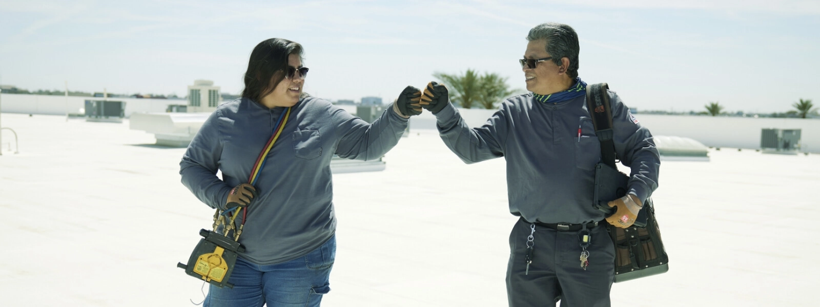 Two HVAC service technicians fist bumping an a roof top